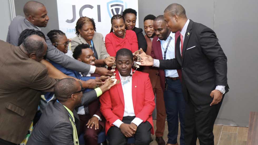 CHAINED: Past presidents of Junior Chamber International (JCI) jointly places the Presidential chain on Dr. Farin Williams (seated) after he was elected as the new JCI National President. During JCI Jamaica annual convention at the Grand Palladium Resort & Spa in Lucea, Hanover on Sunday, October 4. He will assume office on January 1, 2027.  – Photo Derrick Scott