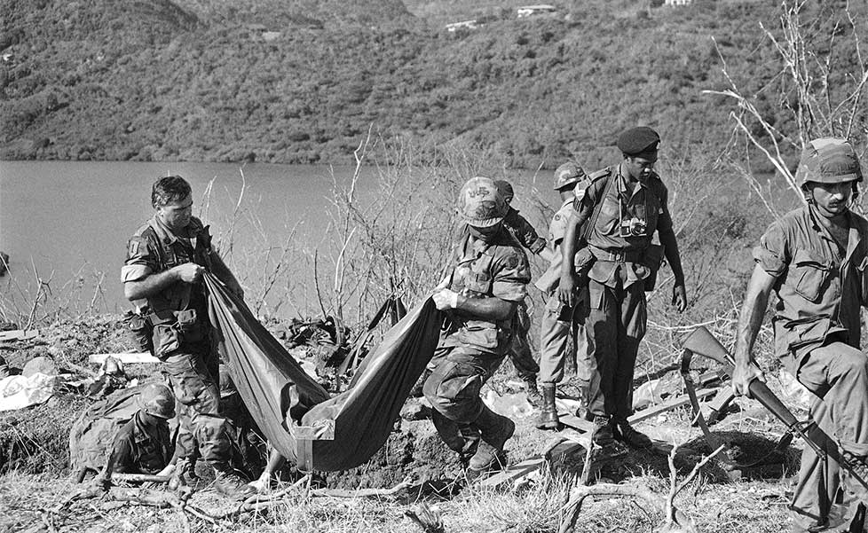 Following the U.S. invasion of Grenada, members of the U.S. Army carry a body bag containing the remains of one of three to four bodies found in a shallow grave at the Calivigny, Grenada military training compound on Nov. 9, 1983. The grave was found on a tip by a civilian who said he saw the bodies of former Grenadian Prime Minister Maurice Bishop and three others being buried. | Pete Leabo / AP